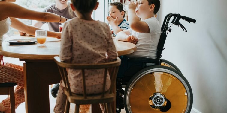 Child in wheelchair eating with family.