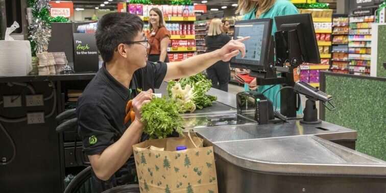 Image of a staff member in a wheelchair at Woolworths happily serving a customer.